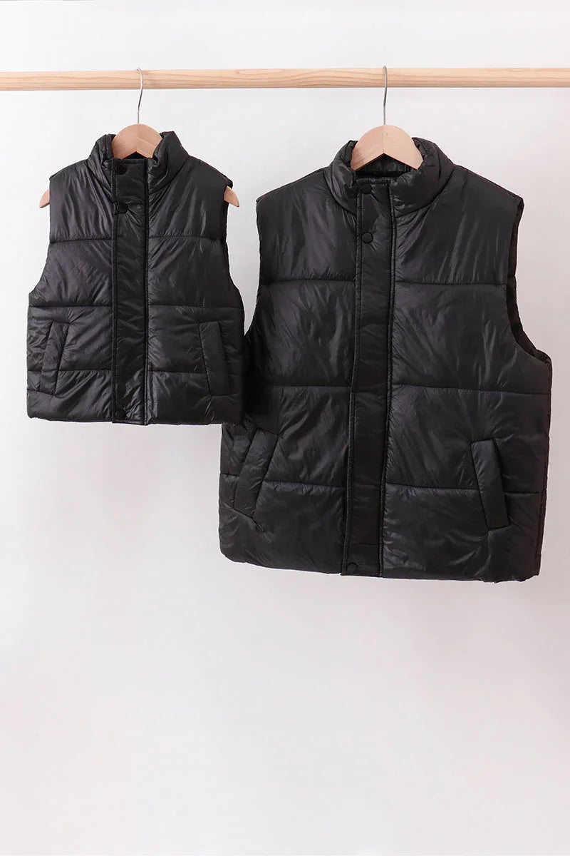 Two black puffer vests hanging on a rack against a white background