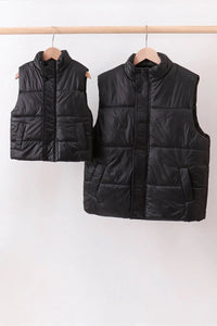 Two black puffer vests hanging on a rack against a white background