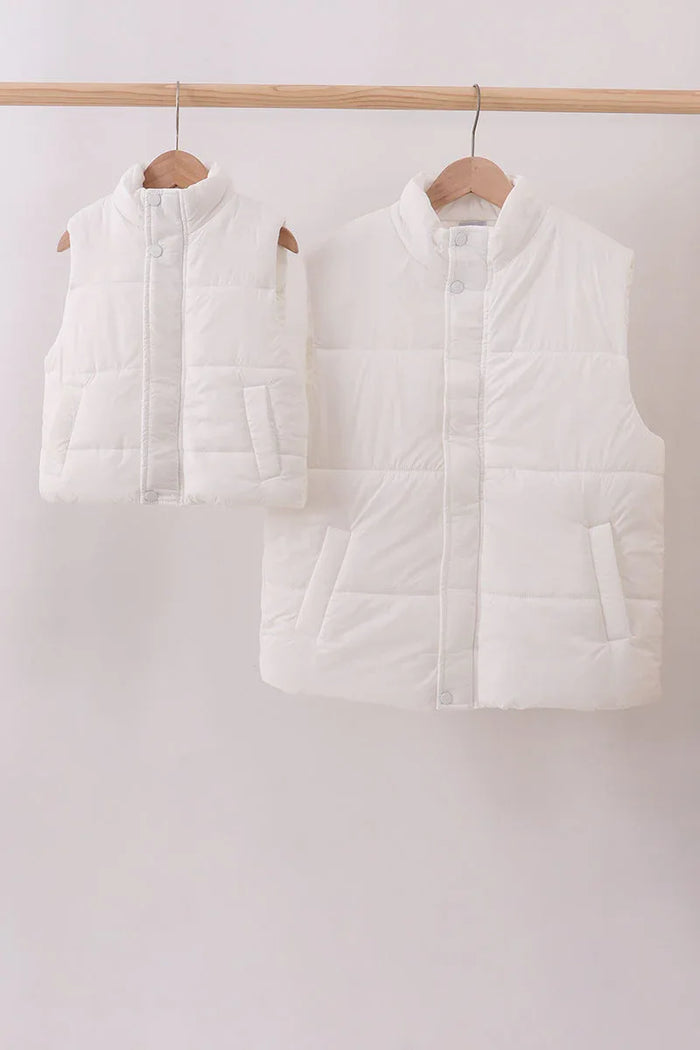 Two white puffer vests hanging on wooden hangers against a white background